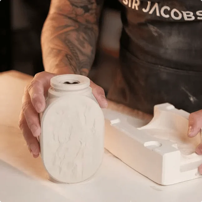 A maker lifting a freshly cast porcelain vessel from its plaster mould
